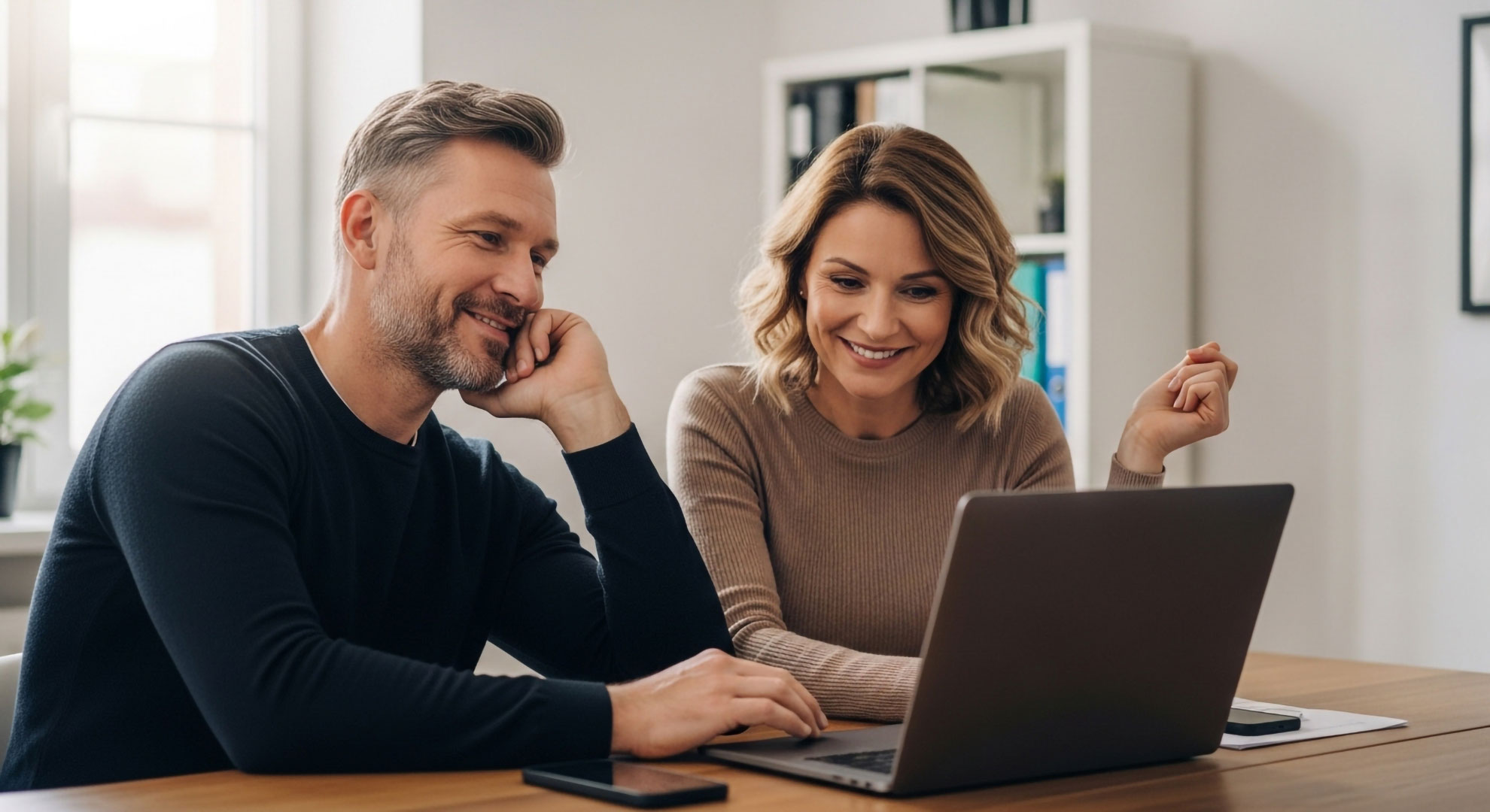Zwei zufriedene Unternehmer, ein Mann und eine Frau, freuen sich am Laptop über den Erfolg und den gestiegenen Umsatz ihrer neuen Website.