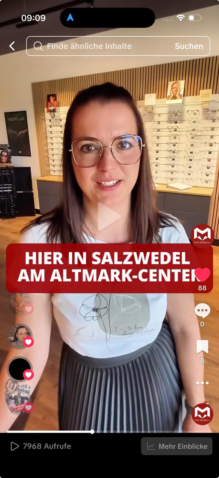Optikerin in Salzwedel spricht vor Brillenregal in die Kamera; Standort am Altmark-Center; lokales Display Marketing mit viel Laufkundschaft.