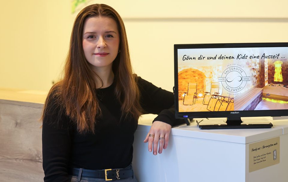 Brigitta Enns steht in der Salzgrotte Salzwedel neben einem digitalen Werbedisplay von Fox Medien für lokales Marketing.