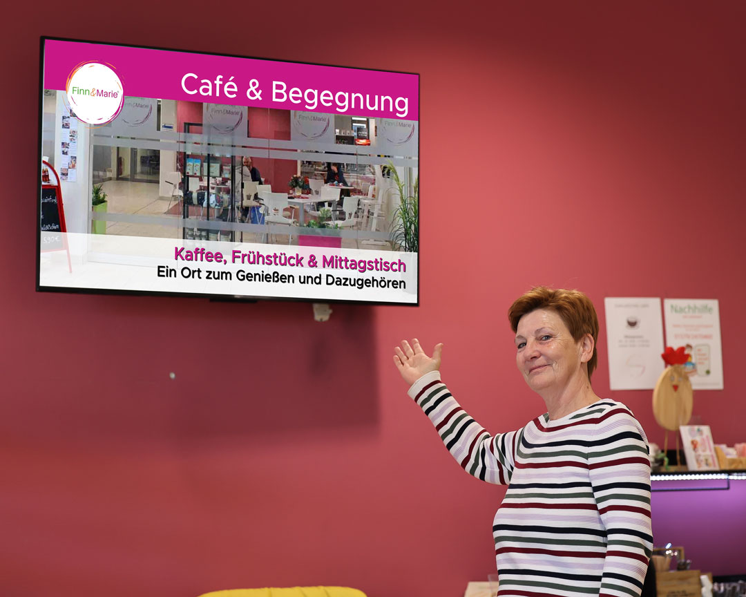 Mitarbeiterin im Inklusionscafé Finn & Marie zeigt auf ein digitales Werbedisplay von Fox Medien in der Elbe-Jeetzel-Klinik Dannenberg.